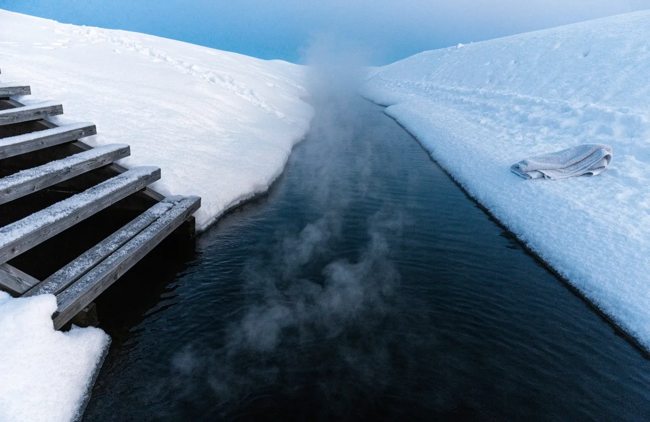 Steam rising from a hole cut in lake ice beside a snow bank